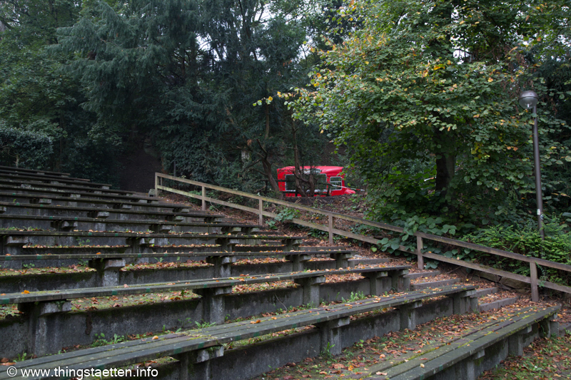 Sitzbänke für das Publikum des Amphitheaters mit Natur und rotem Bus im Hintergrund